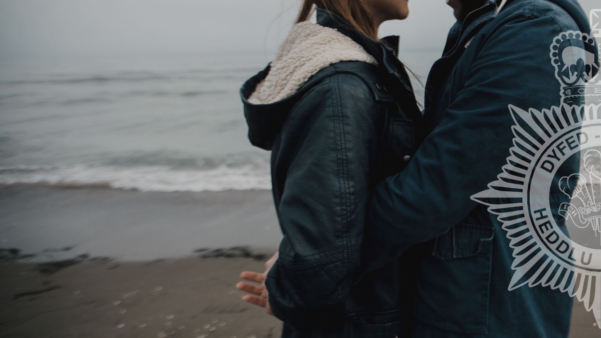 A generic photo of a couple standing on a beach wearing dark raincoats, with the sea in the background