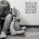 Stock image of a child sitting on the floor holding a teddy bear with one arm