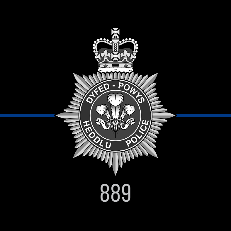 A black and white Dyfed-Powys Police badge on a black background with a thin blue line and the collar number of Sgt Lynwen Thomas