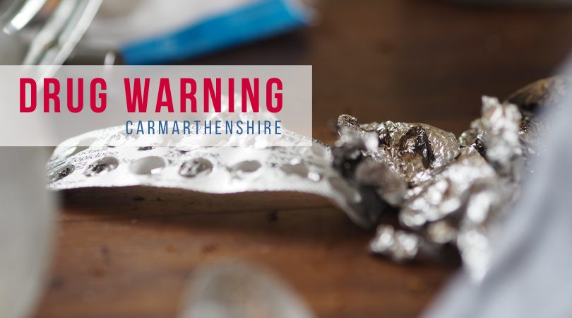 Image of open blister packs in the background on a table, and the words "drug warning - Carmarthenshire" in the foreground