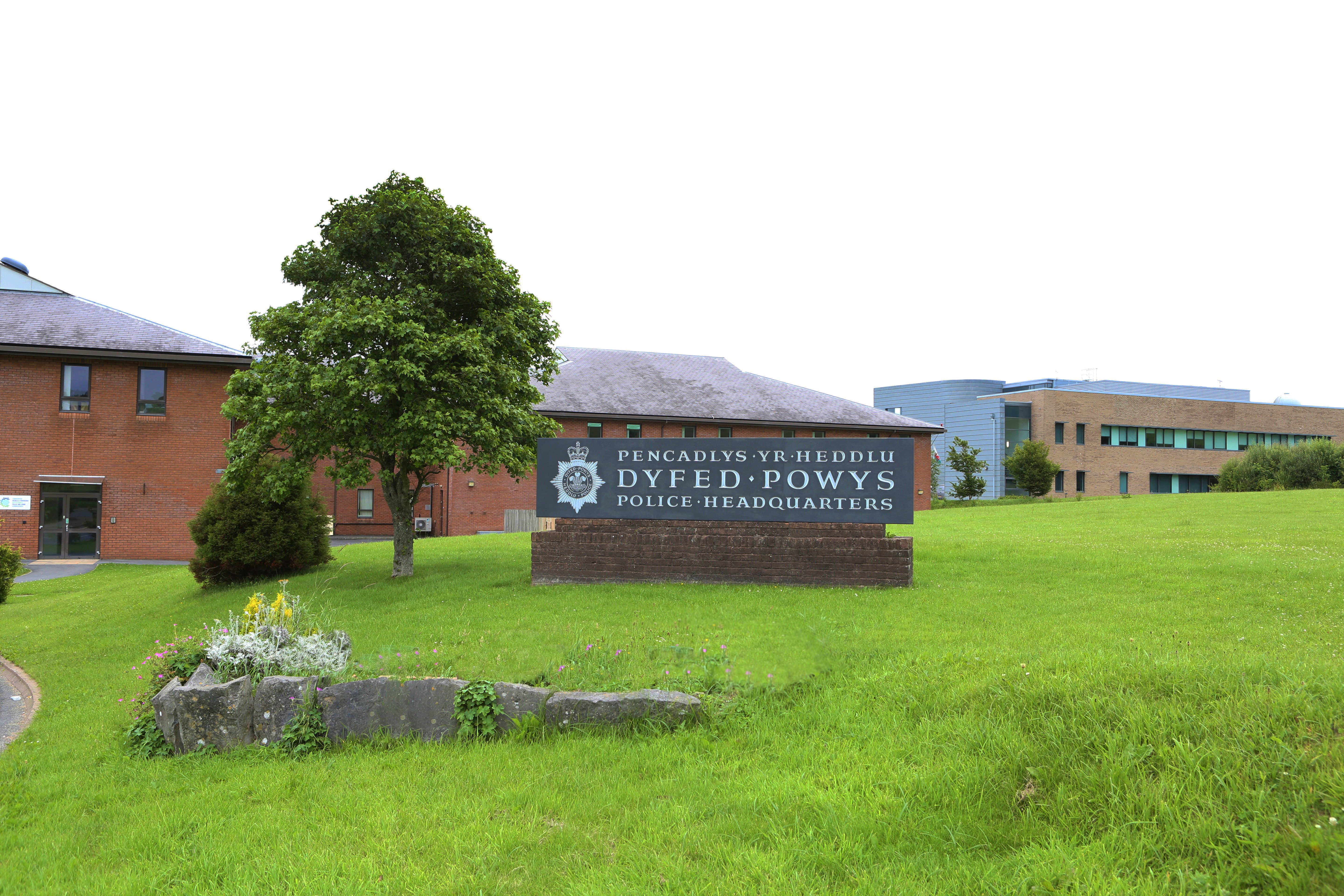 Slate sign at the entrance to Dyfed-Powys Police Headquarters, with two buildings in the background, 