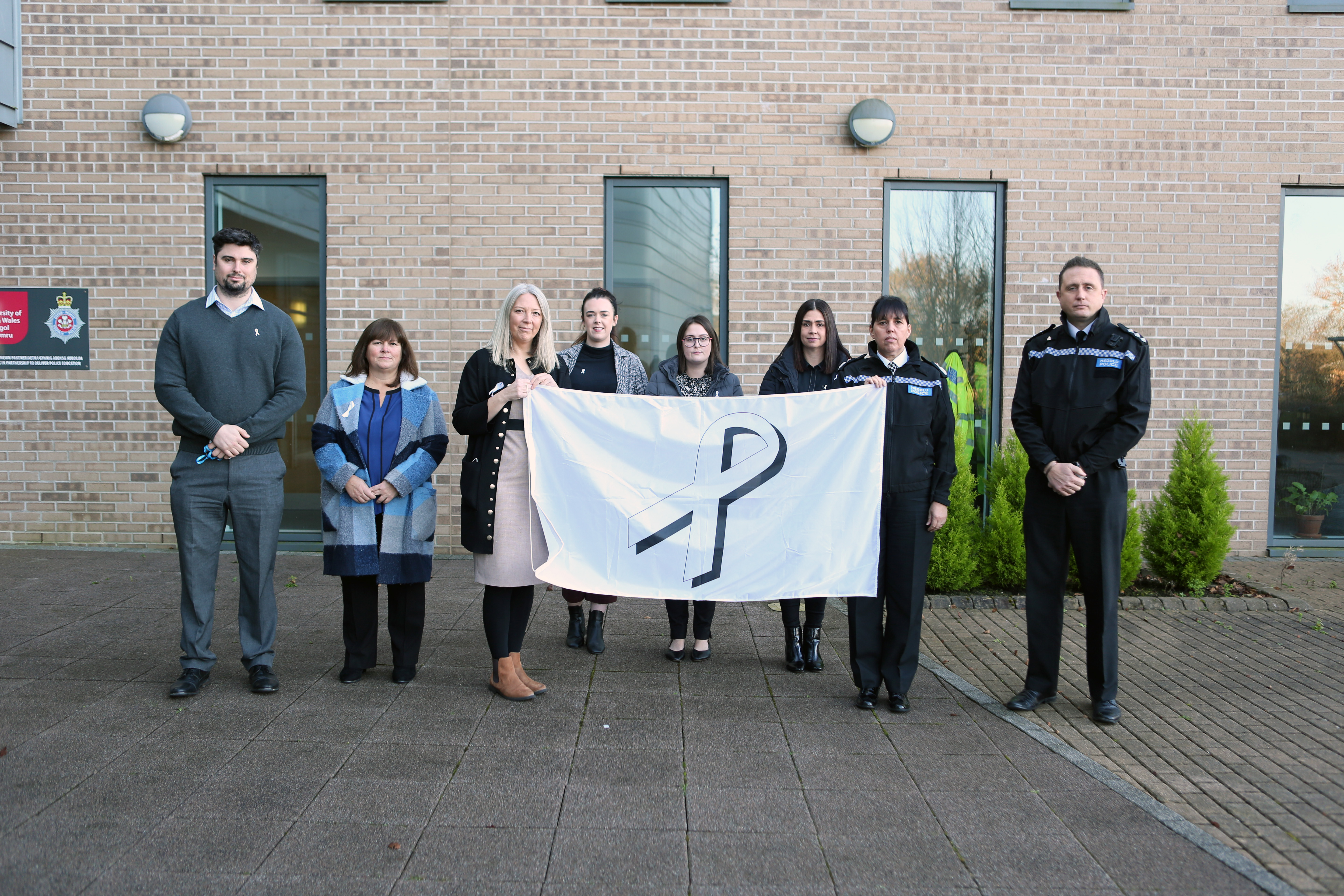 T/Chief Constable Claire Parmenter, Ch/Insp Chris Neve, DI Delyth Evans, and staff from Goleudy, Secondary Risk Assesment Unit and Multi-agency risk assessment conference holding the White Ribbon flag