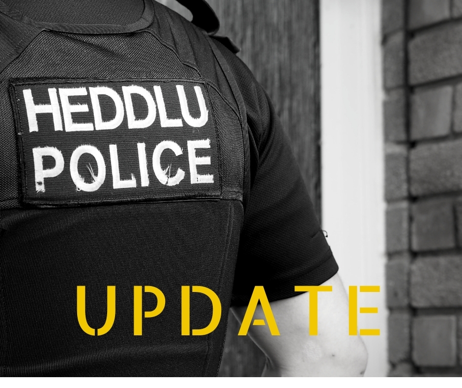 black and white photo back of an officer with Heddlu Police, and in yellow letters underneath the word UPDATE