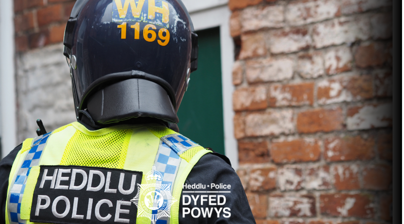 Swyddog heddlu yn gwisgo dillad amddiffynnol a helmed
